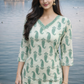 Woman wearing a green and white patterned top by a body of water with a scenic background.