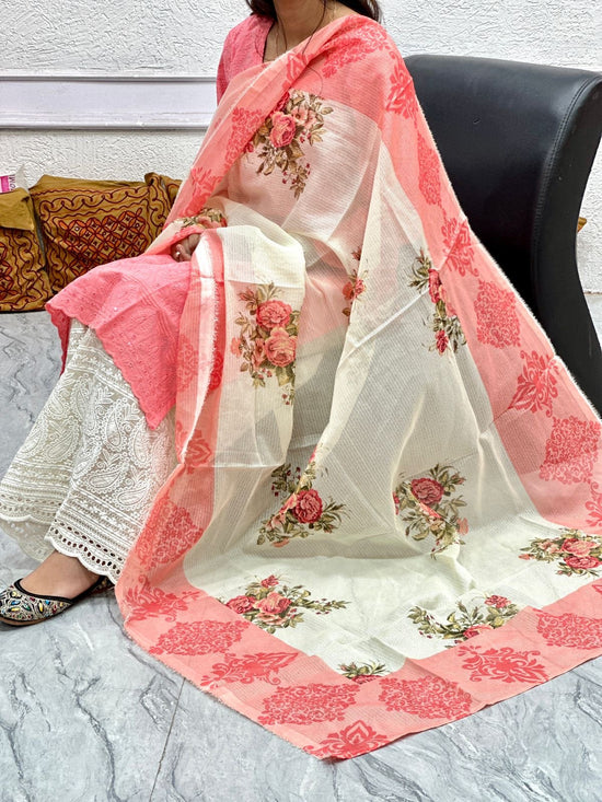 Woman wearing a white saree with pink floral patterns on a light gray floor.
