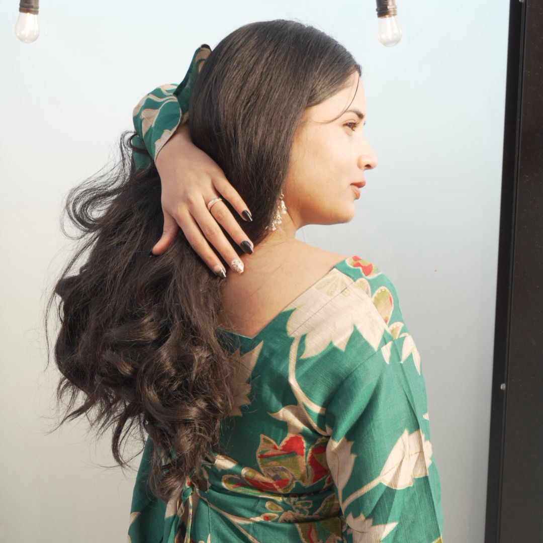 Woman with long hair wearing a green floral dress against a neutral background