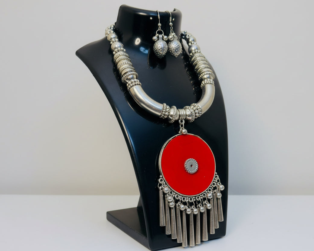 Silver necklace with a red center and matching earrings on a black stand.