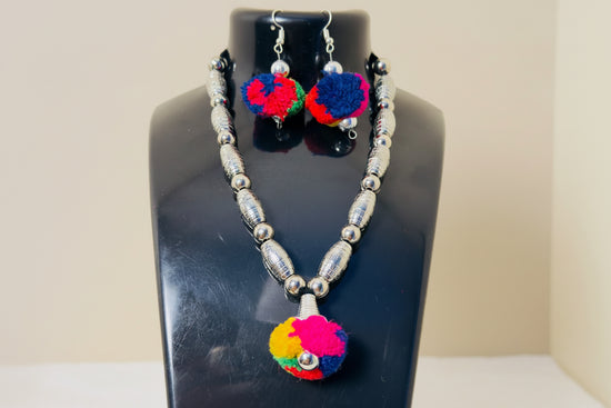 Necklace and earrings with colorful pom-poms on a black stand.