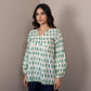 Mannequin wearing a green and white patterned top with navy pants against a beige wall.