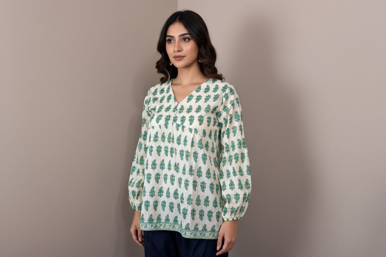 Mannequin wearing a green and white patterned top with navy pants against a beige wall.