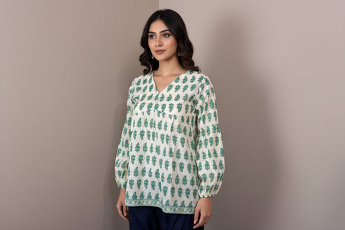 Mannequin wearing a green and white patterned top with navy pants against a beige wall.